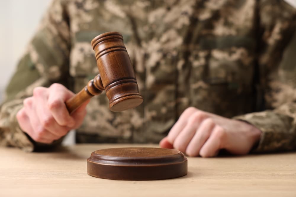 A close-up of a man in a military uniform sitting at a wooden table, his hand resting on a gavel.