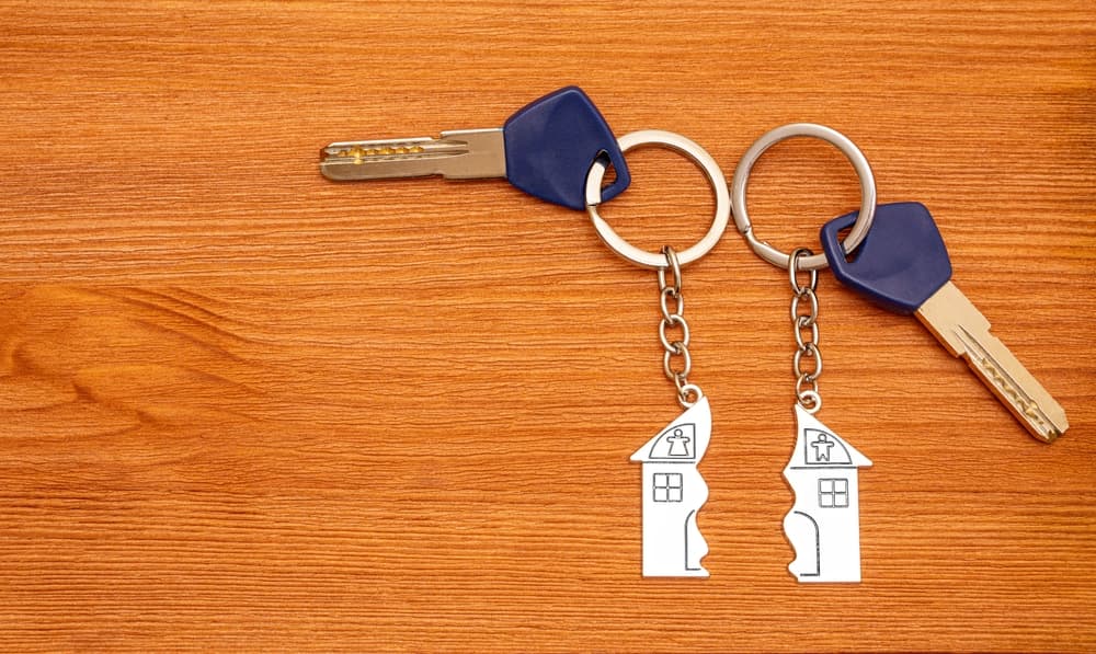 Two keys with split house matching keychains on a wooden table. Splitting assets in a divorce.